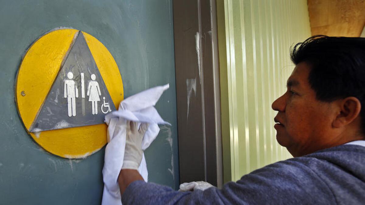 Edgar Lopez, un trabajador de mantenimiento de West Hollywood, limpia las puertas del baño en Plummer Park, el año pasado, meses antes de que se requieran instalaciones de género neutro en sitios y negocios de la ciudad.