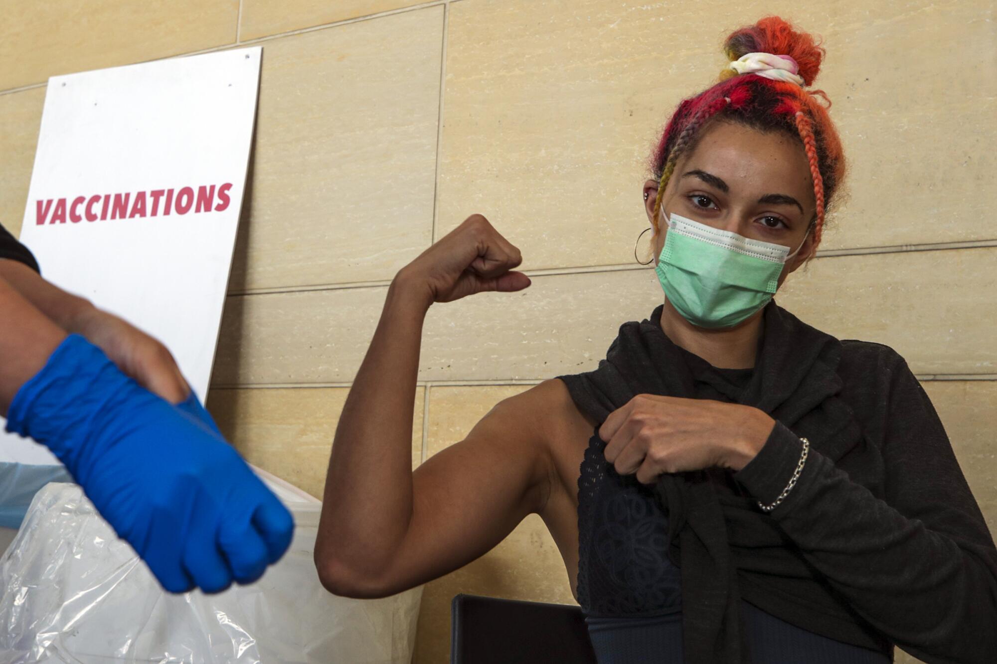 A woman wearing a mask flexes her bicep