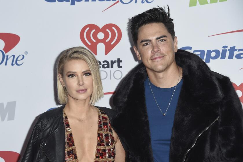 Ariana Madix in a black leather jacket and deep cut dress standing next to, Tom Sandoval in a blue shirt and black fur jacket