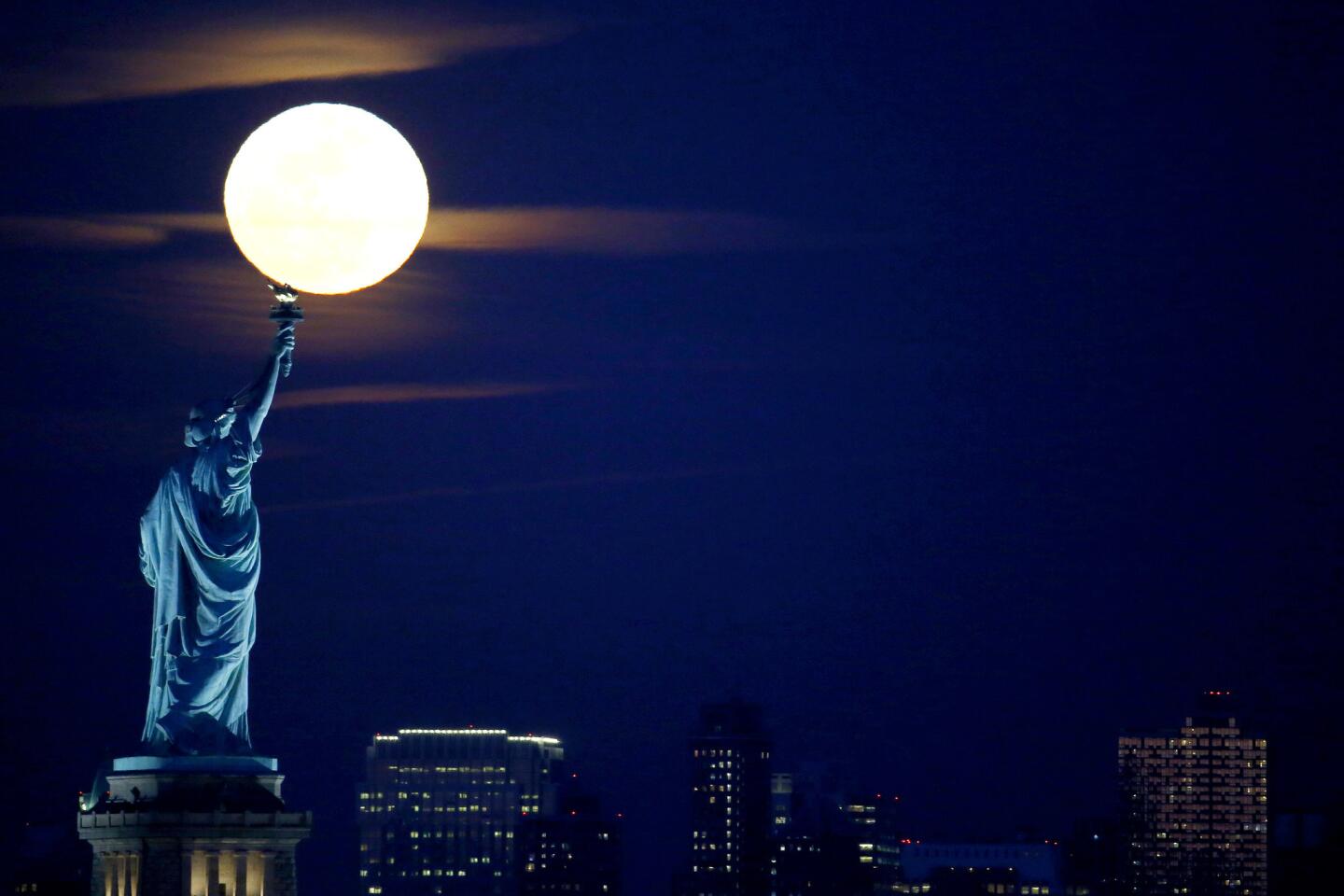 A full moon rises over the Statue of Liberty seen from the Port Liberte neighborhood of Jersey City, N.J.