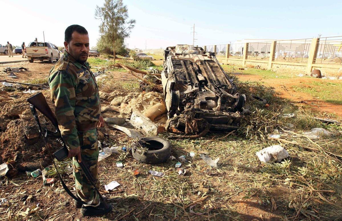 A member of the Libyan security forces stands next to a burnt-out vehicle Sunday after a suicide bombing outside Benghazi in eastern Libya.