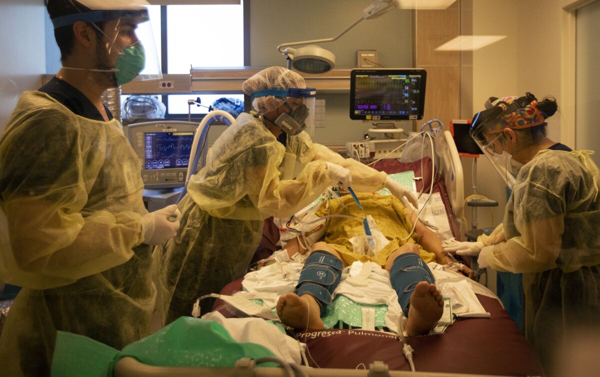 Nurses in full protective gear work on a COVID-19 patient in a hospital bed