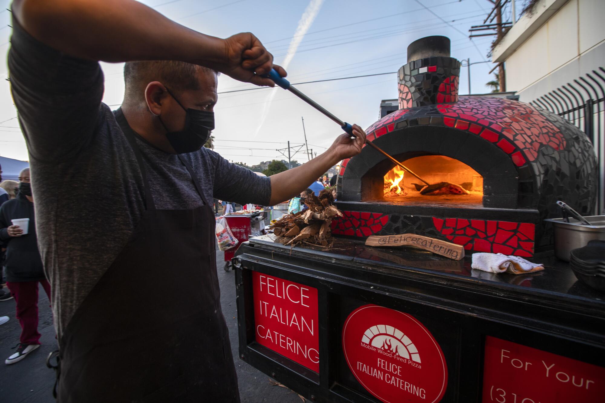A man checks on a pizza in a wood-fired oven.