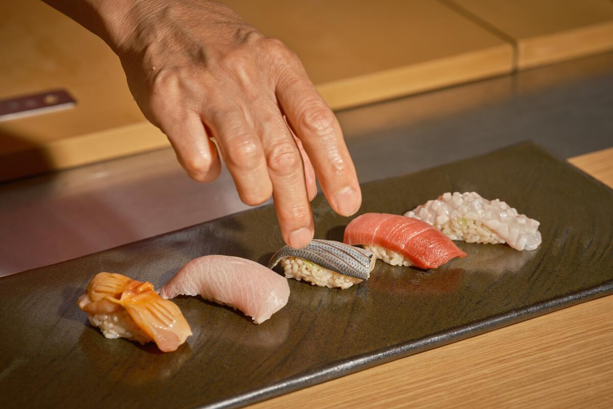A hand extends to place sushi on a flat plate.