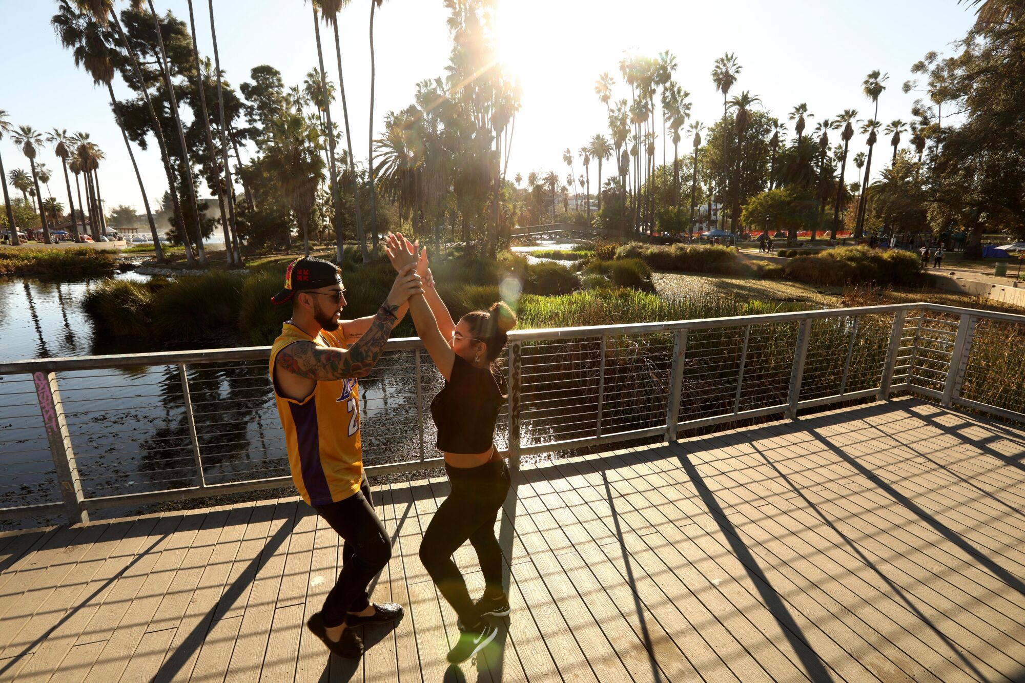 A man in a Lakers jersey and a woman dance on a platform next to a lake
