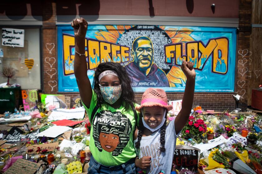 MINNEAPOLIS , MINNESOTA - JUNE 01: Two girls with fist raised pay their respects at the makeshift memorial for George Floyd at intersection in front Cup Foods where Floyd was murdered by a Minneapolis police officer on Monday, June 1, 2020 in Minneapolis , Minnesota. (Jason Armond / Los Angeles Times)