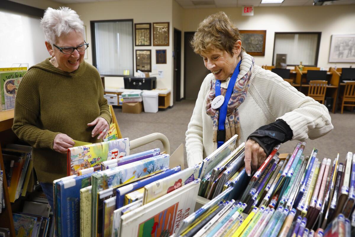 Volunteers Barbara Sutton and Diane Davis organize a cart of children’s books at the JCC library.