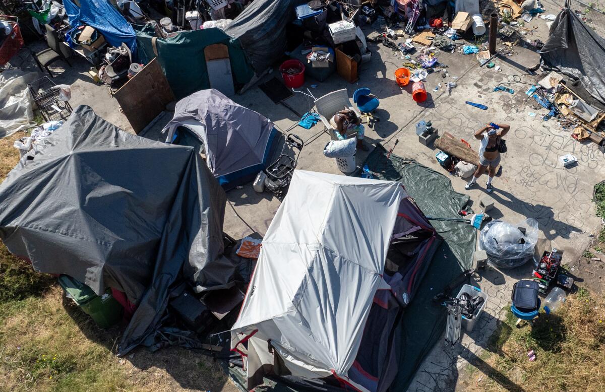 An aerial view of several tents and makeshift shelters, surrounded by buckets and other objects on a concrete surface