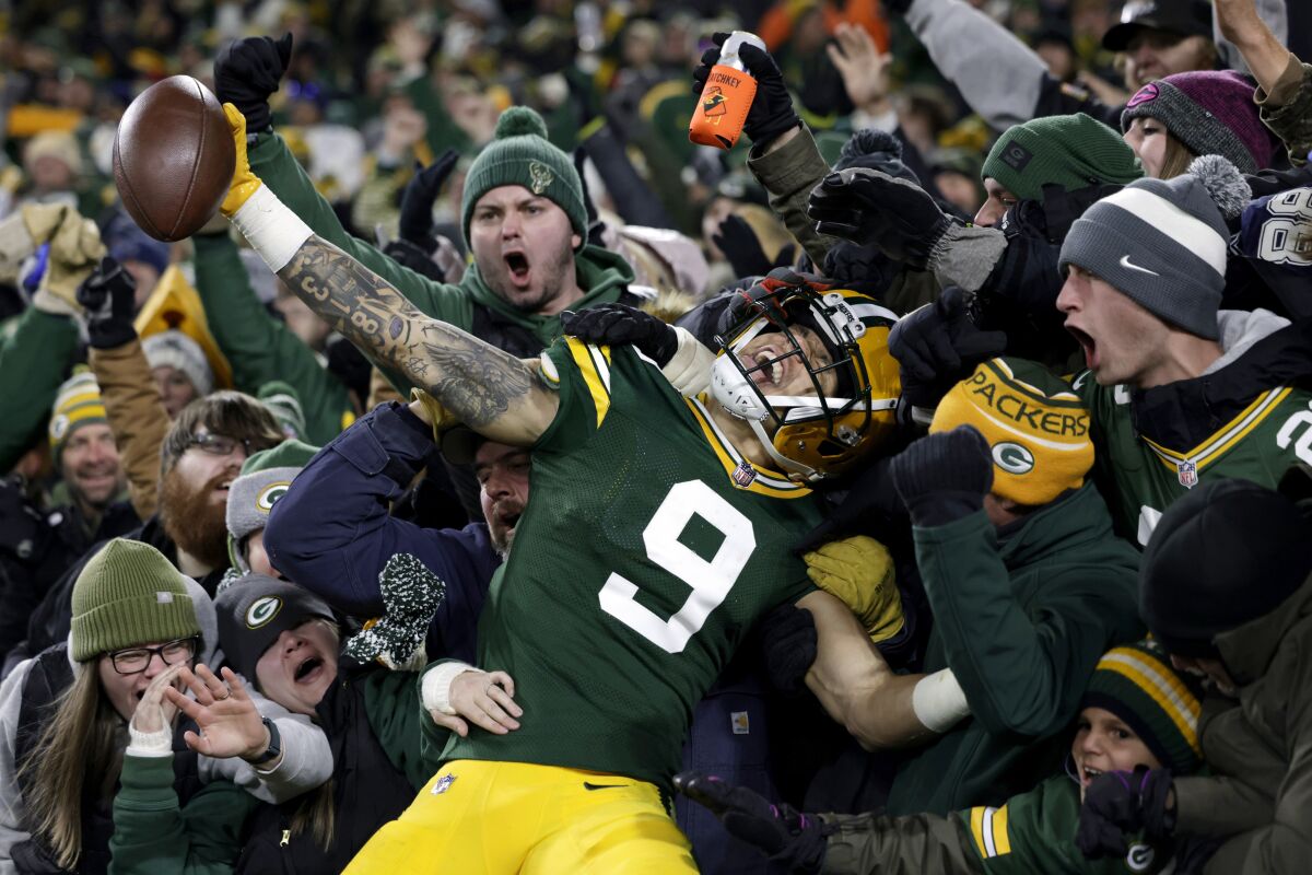 Christian Watson does Lambeau Leap after scoring a TD