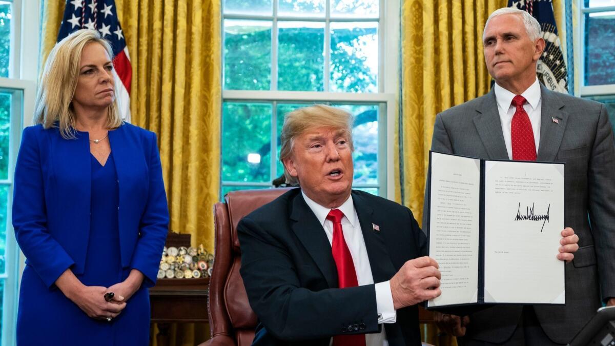 President Trump, flanked by Homeland Security Secretary Kirstjen Nielsen, left, and Vice President Mike Pence, displays the executive order he signed Wednesday reversing his own family separation policy at the border.