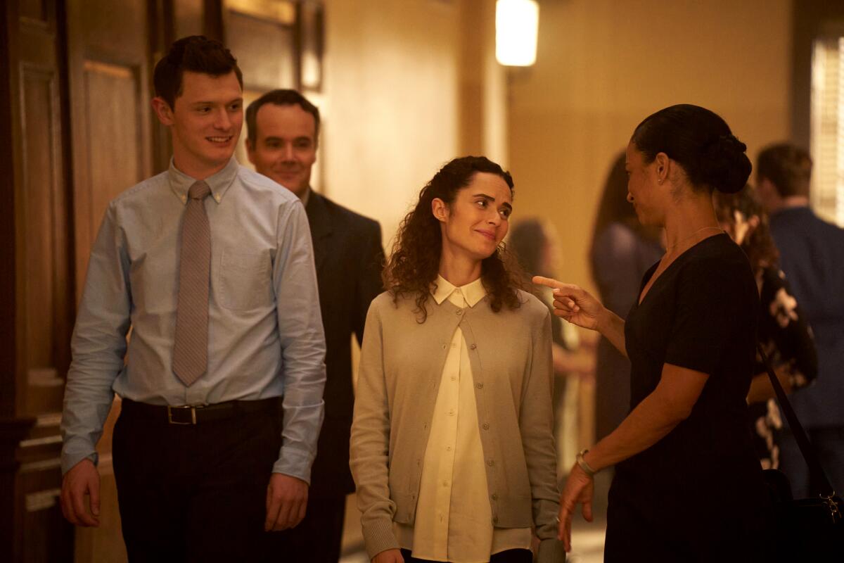 Four people walk down a hallway looking at each other