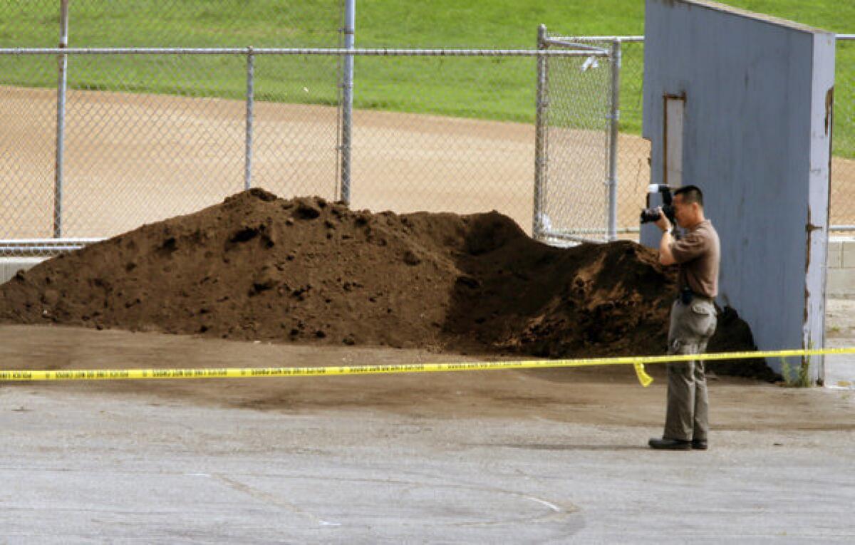 An investigator takes pictures near an athletic field in Manhattan Beach where the body was found last week.