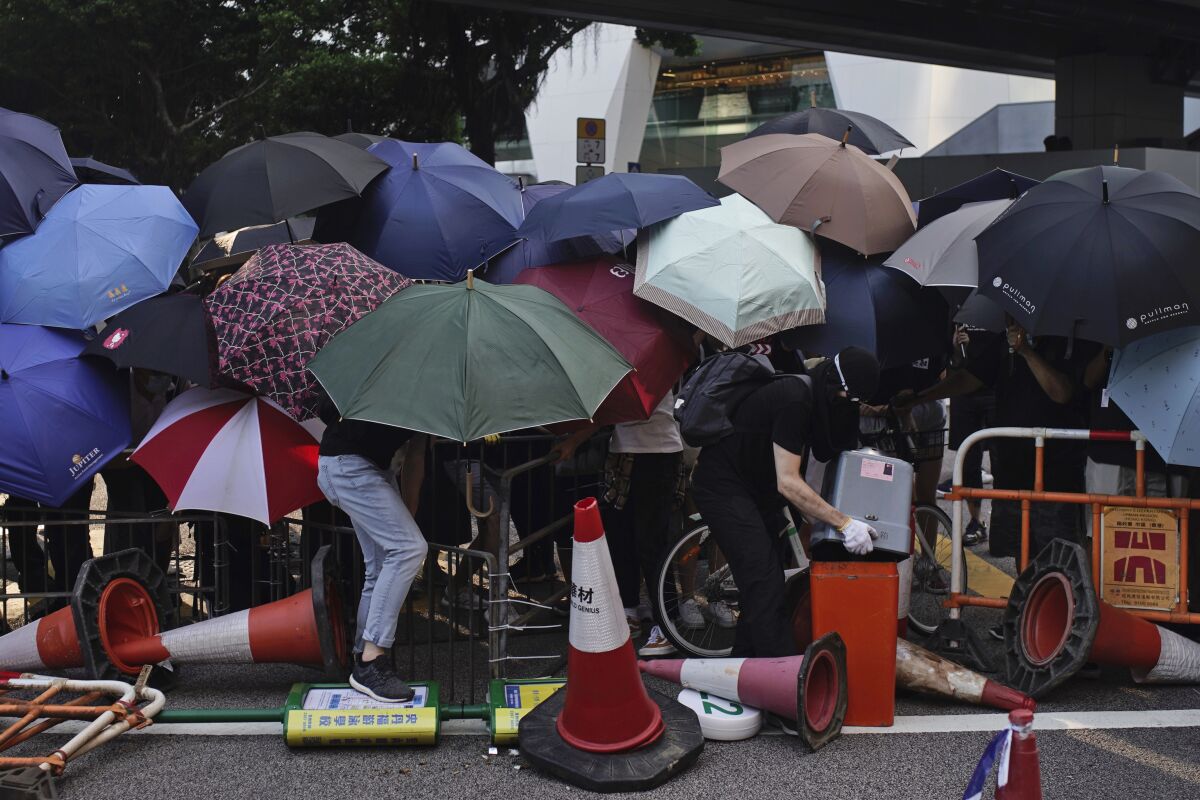Protesters hide behind umbrellas as they form a barricade to block a road in Hong Kong on Friday, Oct. 4, 2019. Thousands of protesters in masks are streaming into Hong Kong streets after the territory's leader invoked rarely used emergency powers to ban masks at rallies. (AP Photo/Felipe Dana)