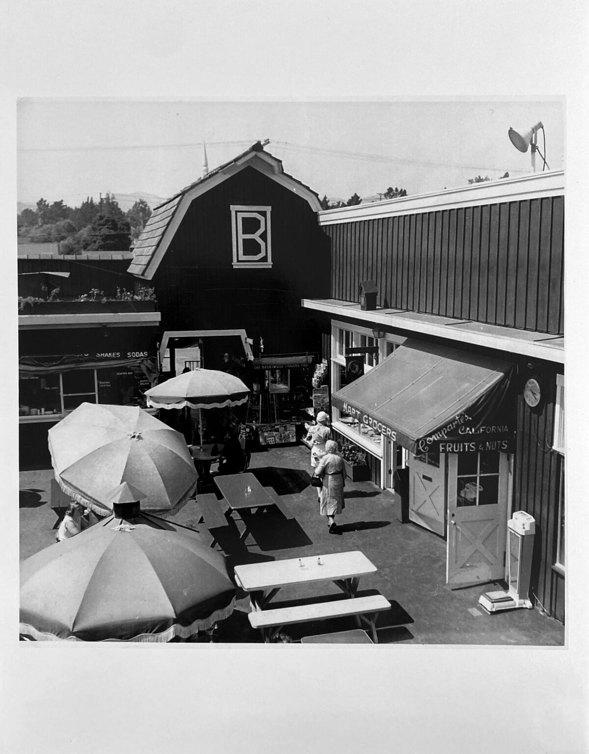 A vintage photo of a building that looks like a barn, with a white B, and tables with umbrellas in front of it.