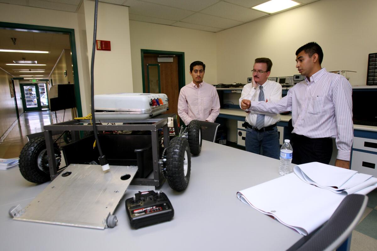 With Glendale Community College's Society of Hispanic Professional Engineers Club vice president Fernando Santana, left, president Jose Martinez, right, explains how a robot created for picking up trash works to Dr. Jeff Smith, instructor of language arts, center, during the school's Manufacturing Day open house on Friday, Oct. 2, 2015.