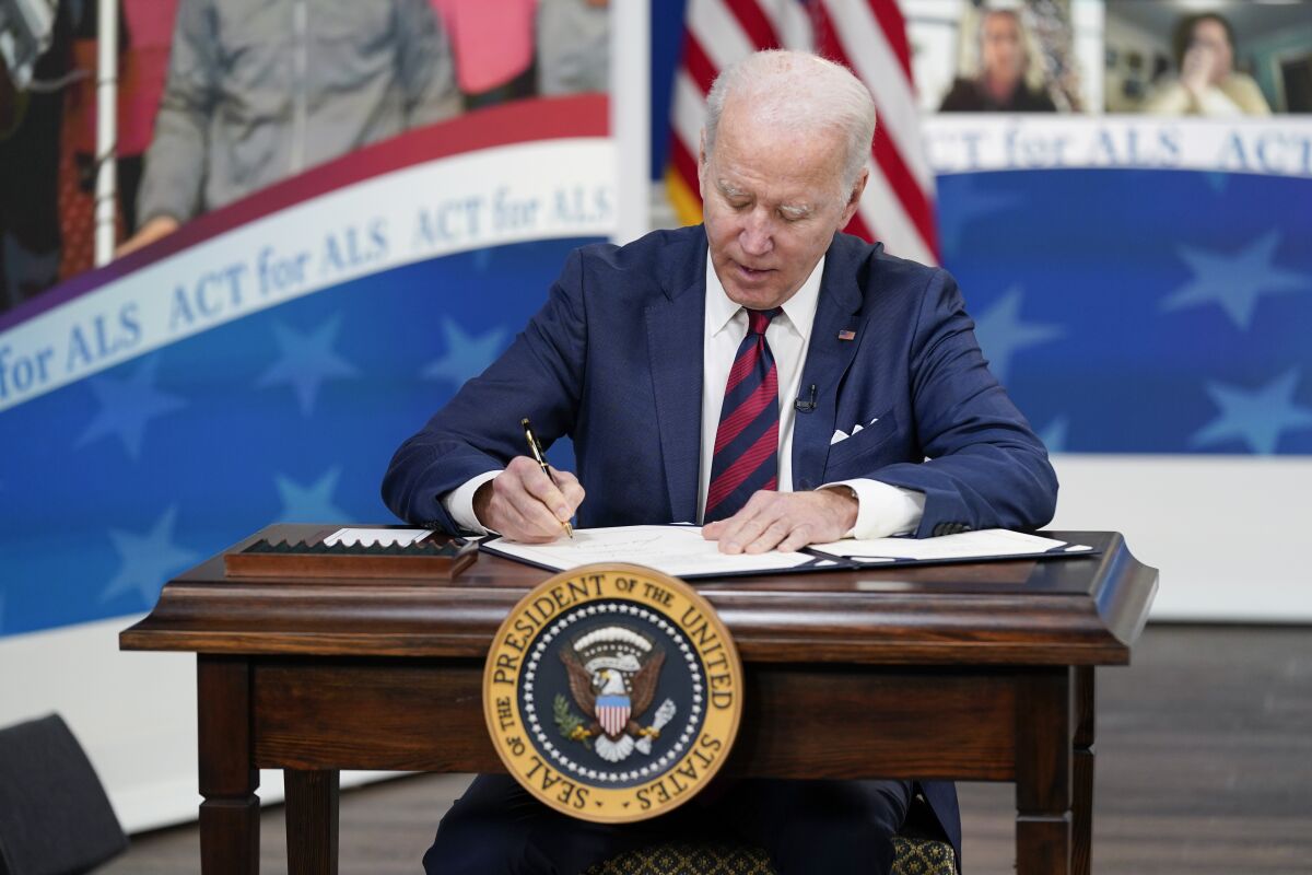 President Biden sits at a desk signing a document