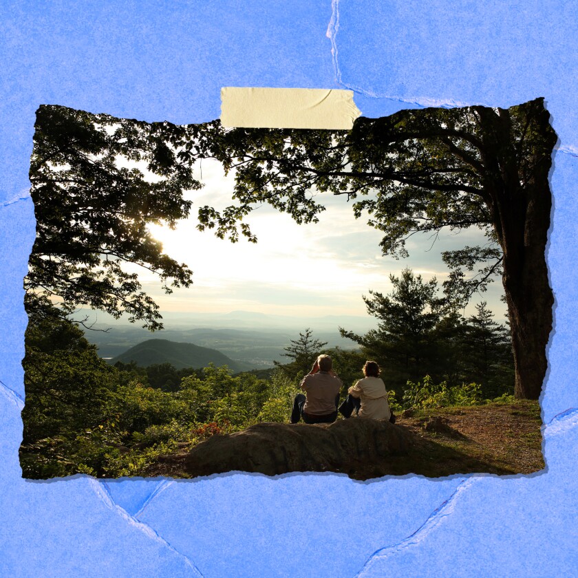 Two people sit in a clearing, looking out at the sky.