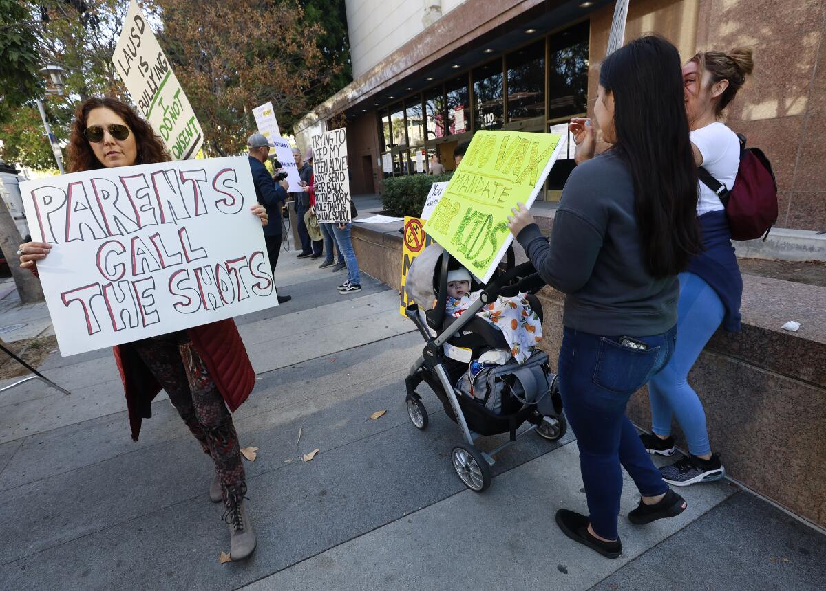 Protestors against an Los Angeles school vaccine mandate hold signs.
