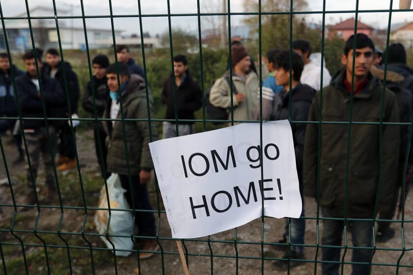 Migrants watch protesters demanding the closure of overcrowded refugee camps and the relocation of migrants from the city area, in front of the Bira refugee camp in Bihac, northwestern Bosnia, Friday, Nov. 15, 2019. A banner that reads: ''IOM (International Organization for Migration) go home!'' While many Bosnians have expressed sympathy with migrants because of their own war experience, many also protested their presence and demanded that migrants be moved or restricted to refugee camps. (AP Photo/Darko Vojinovic)