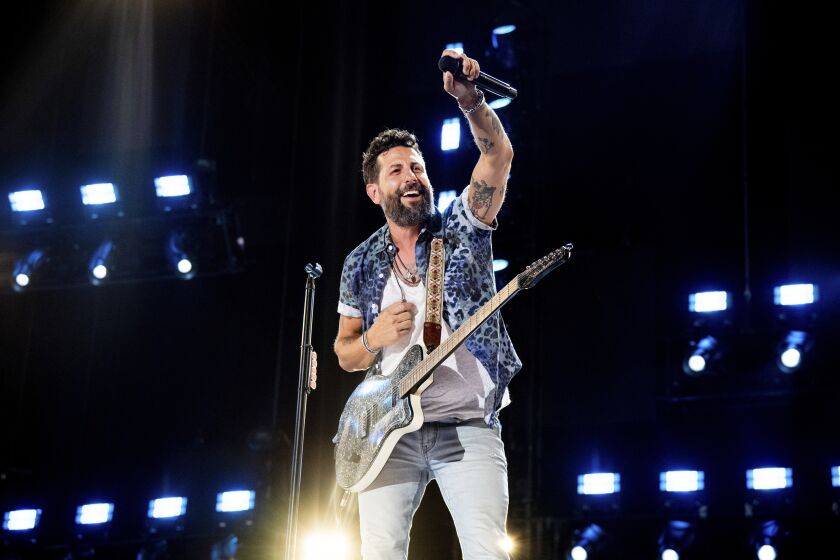Matthew Ramsey of Old Dominion raises his left hand onstage while performing with a guitar 