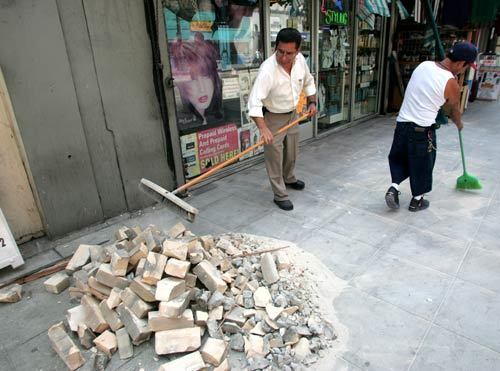 Store owner Hilario Sanchez, left, and Antonio Lopez sweep dust and bricks in front of Goleth's Beauty Salon on Broadway in downtown L.A. after an estimated 5.4 earthquake centered near the Chino Hills area rocked L.A.