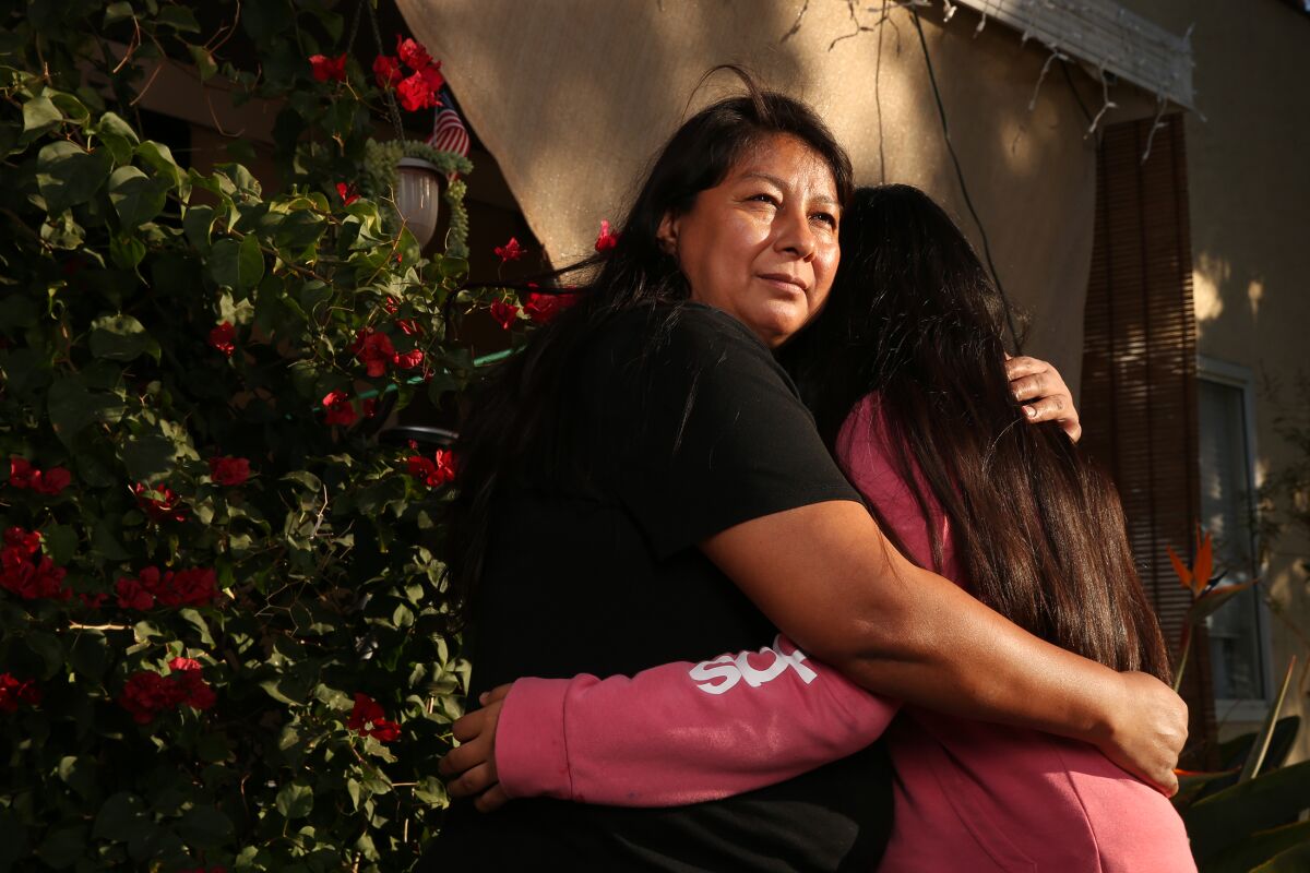 A mother hugs her 13-year-old daughter outside their home