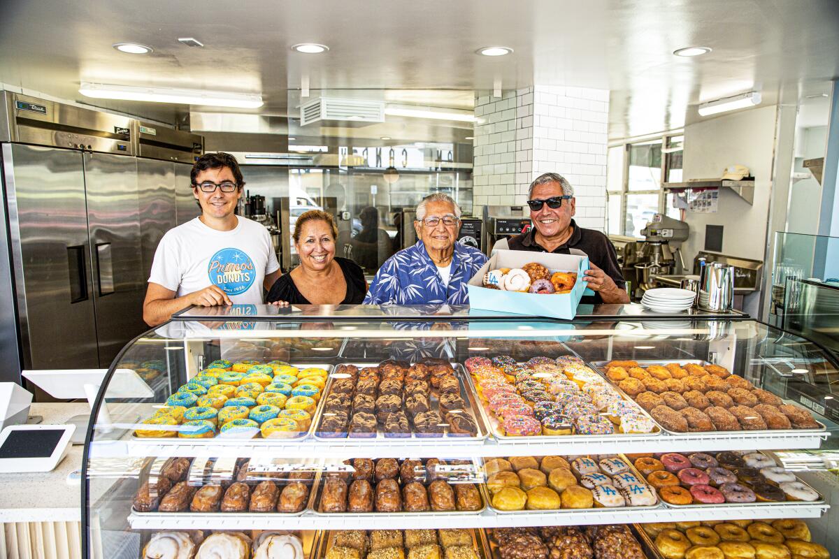Four people stand smiling behind a donut shop counter