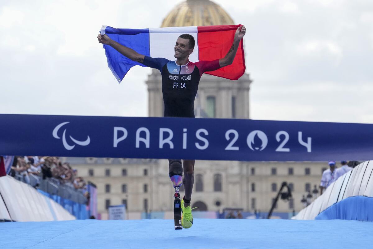 France's Alexis Hanquinquant waves his country's flag as he wins the men's PTS4 Triathlon at the 2024 Paralympics Monday