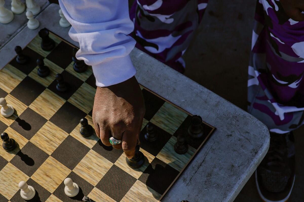 A hand moves a chess piece on a board, as seen from above. 