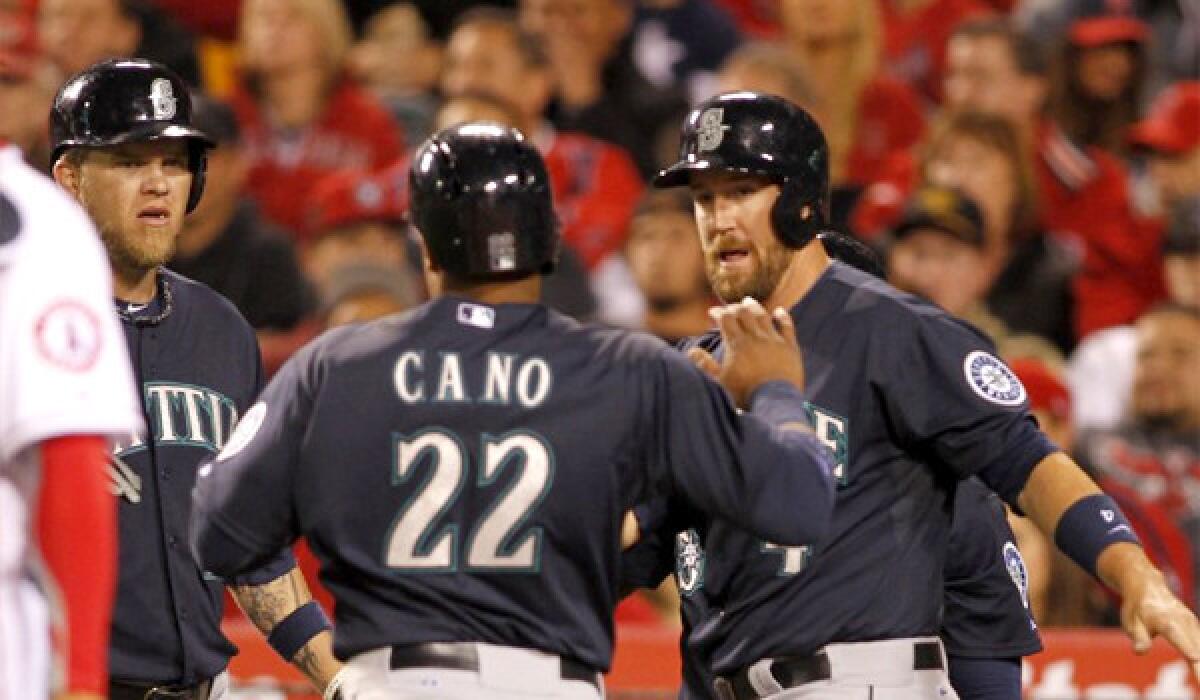 Seattle's Corey Hart, left, and John Buck, right, congratulate Robinson Cano as he scores on a double by Justin Smoak during the third inning of the Angels' 8-3 loss Tuesday to the Mariners.