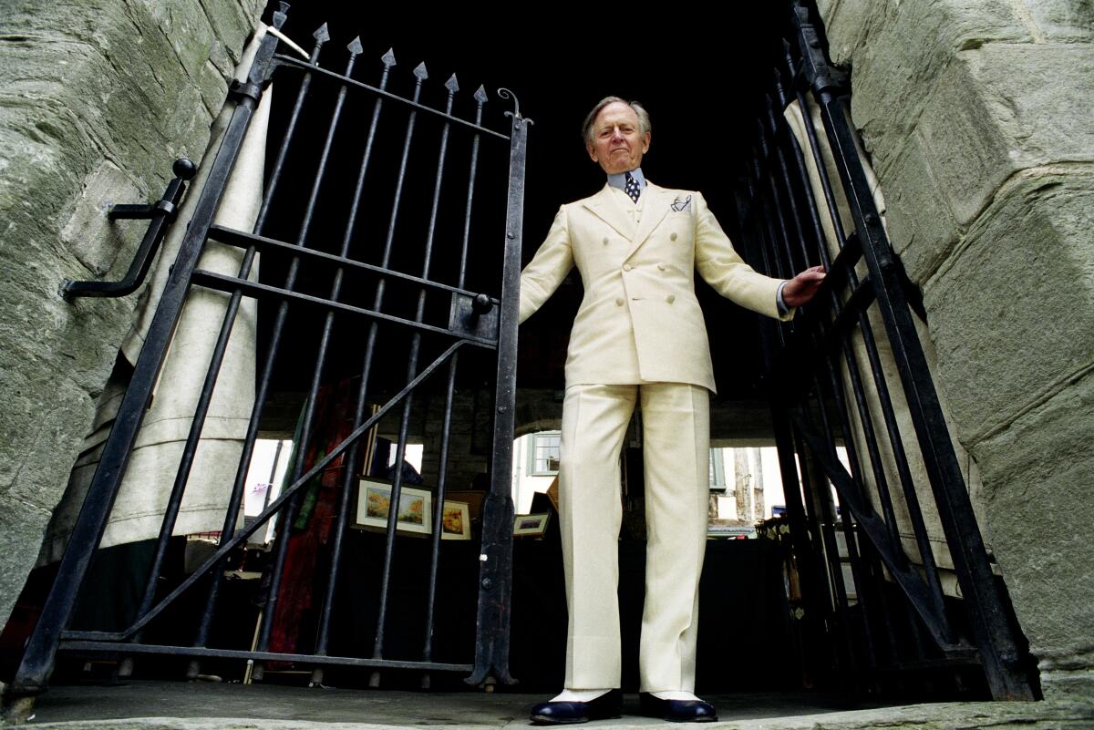 A white-suited man stands at an iron gate.