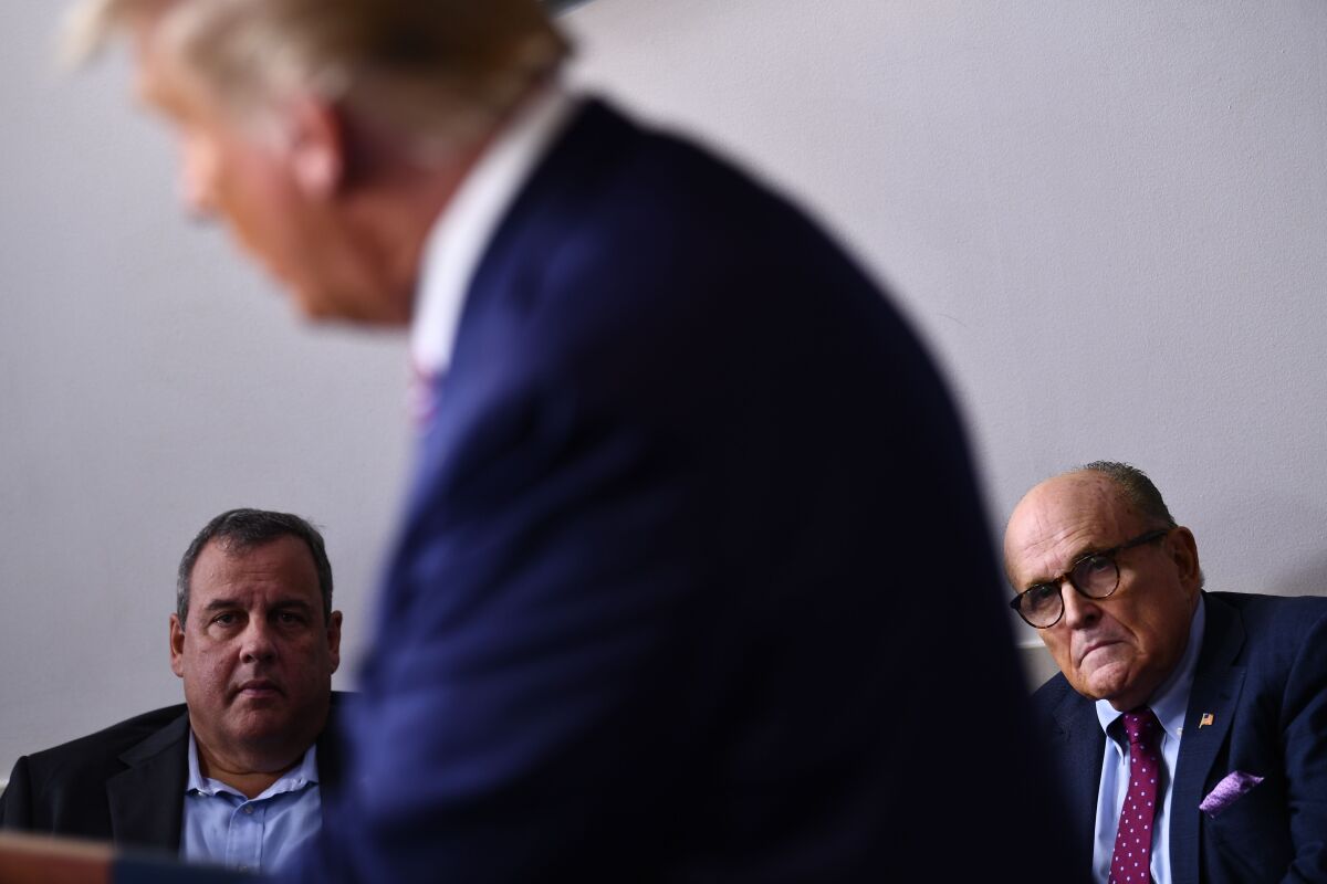 Two men in the background listen while a man in the foreground speaks.
