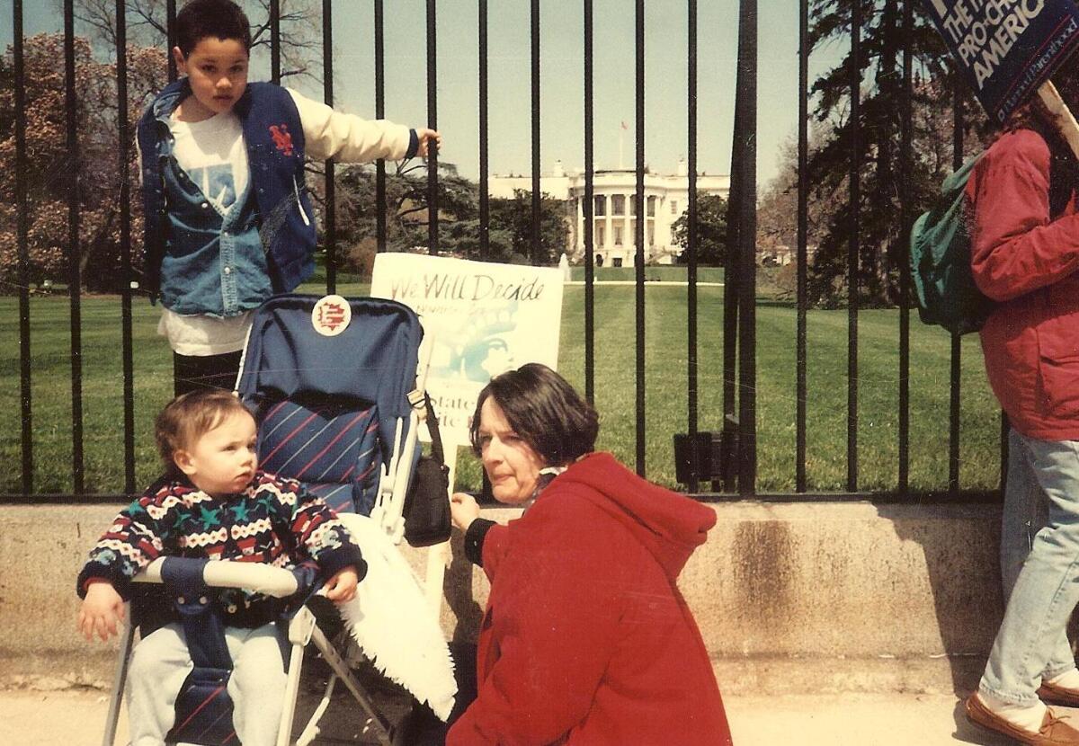 Cari Beauchamp sitting outside of the White House gates in a red sweater with young sons nearby
