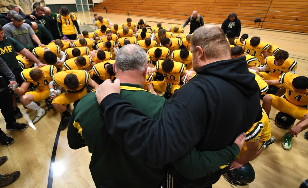 High school team members bow their head with their coaches.