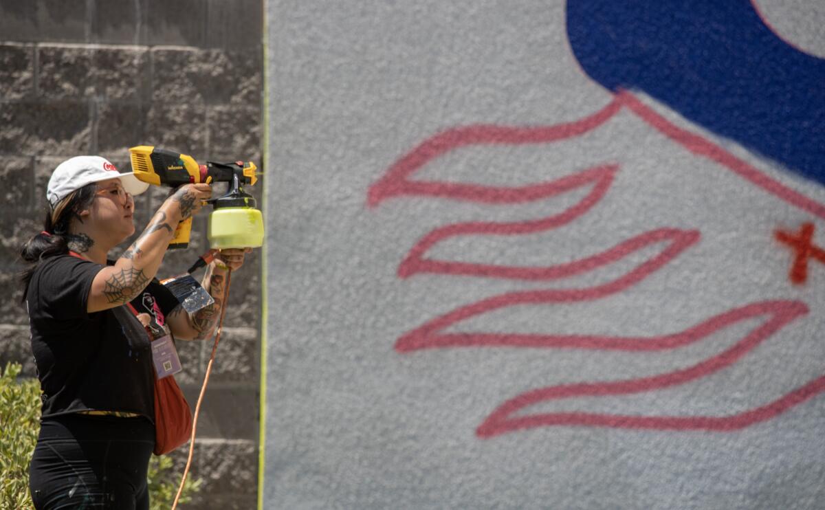 Long Beach Walls artist Stevie Shao sprays paint on a mural in progress on a building at the Renaissance High School.