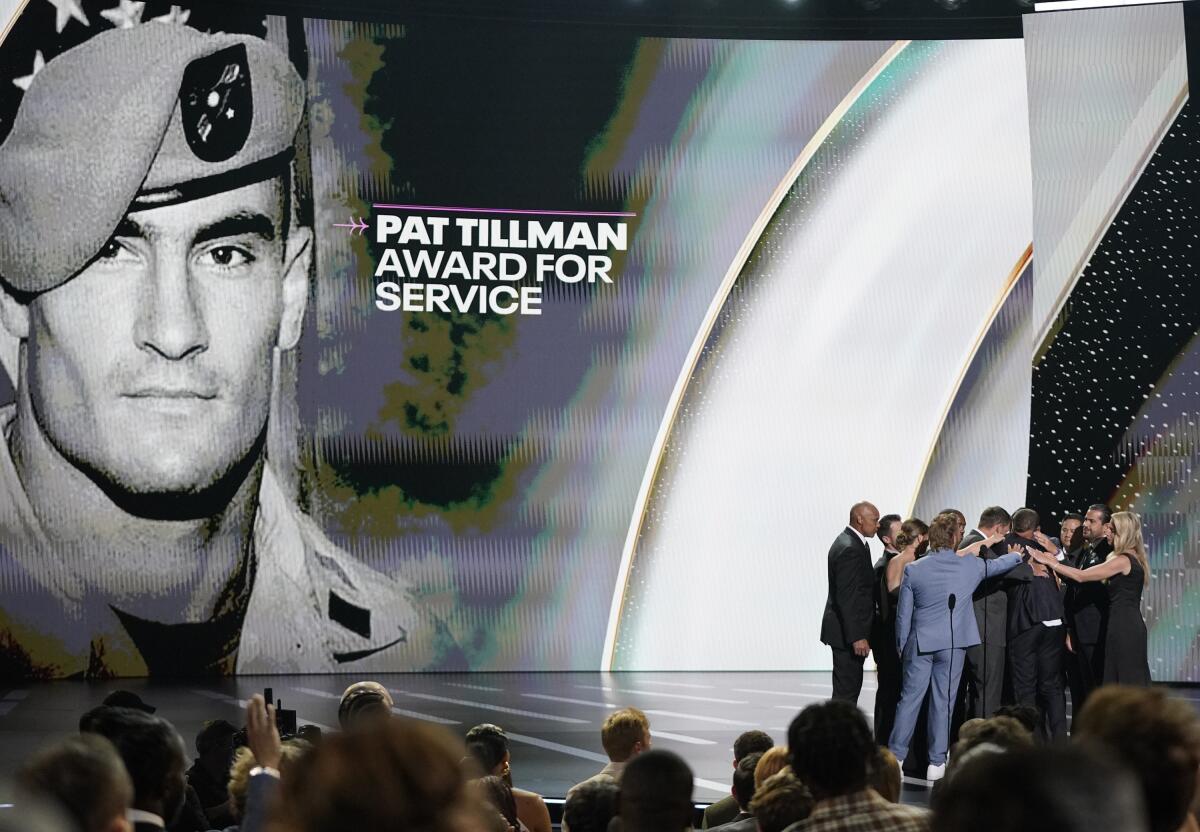 NFL player Damar Hamlin hugs members of the Buffalo Bills training staff in front of a portrait of Pat Tillman in 2023.