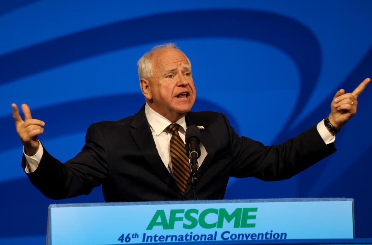 Tim Walz gestures as he speaks against a blue background from a lectern that reads "46th AFSCME International Convention"