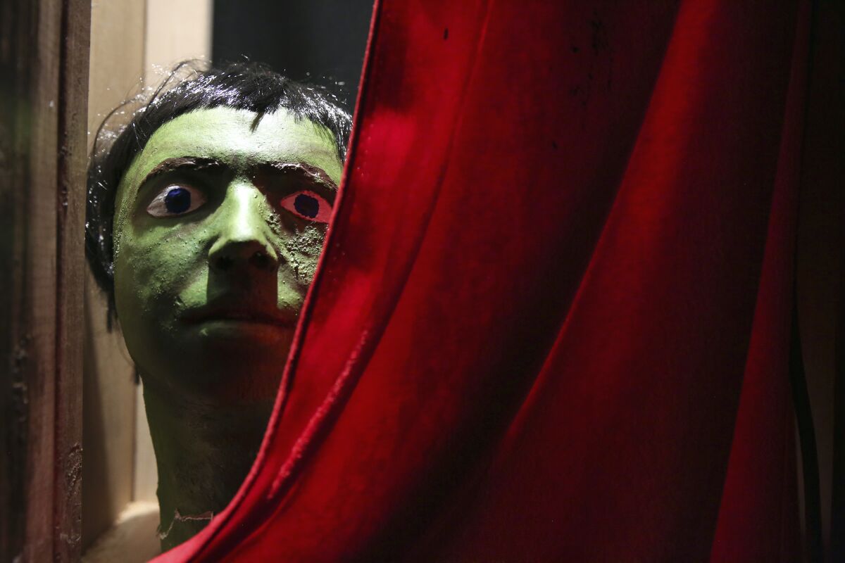 An art installation shows a creepy masked face in green behind a red curtain