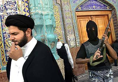 A religious cleric passes by the entrance to the holy Imam Ali Shrine as a hooded Iraqi police officer stands guard after the withdrawal of the Mahdi Army. Some Iraqi police worry they will be targets of violence and prefer to keep their identities hidden.