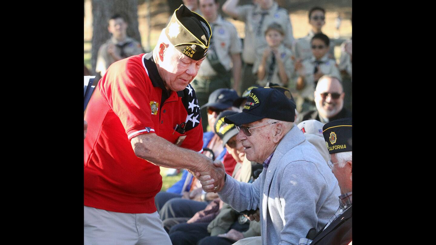 Veteran Jerry Peterson helps honoree veteran Joe Vaccare to his feet to receive a certificate of recognition at Two Strike Park in La Crescenta on Wednesday, November 11, 2015. Boy Scout Troop 288 conducted a community flag burning, as well as speeches by Congressman Adam Schiff and State Congressman Mike Gatto.