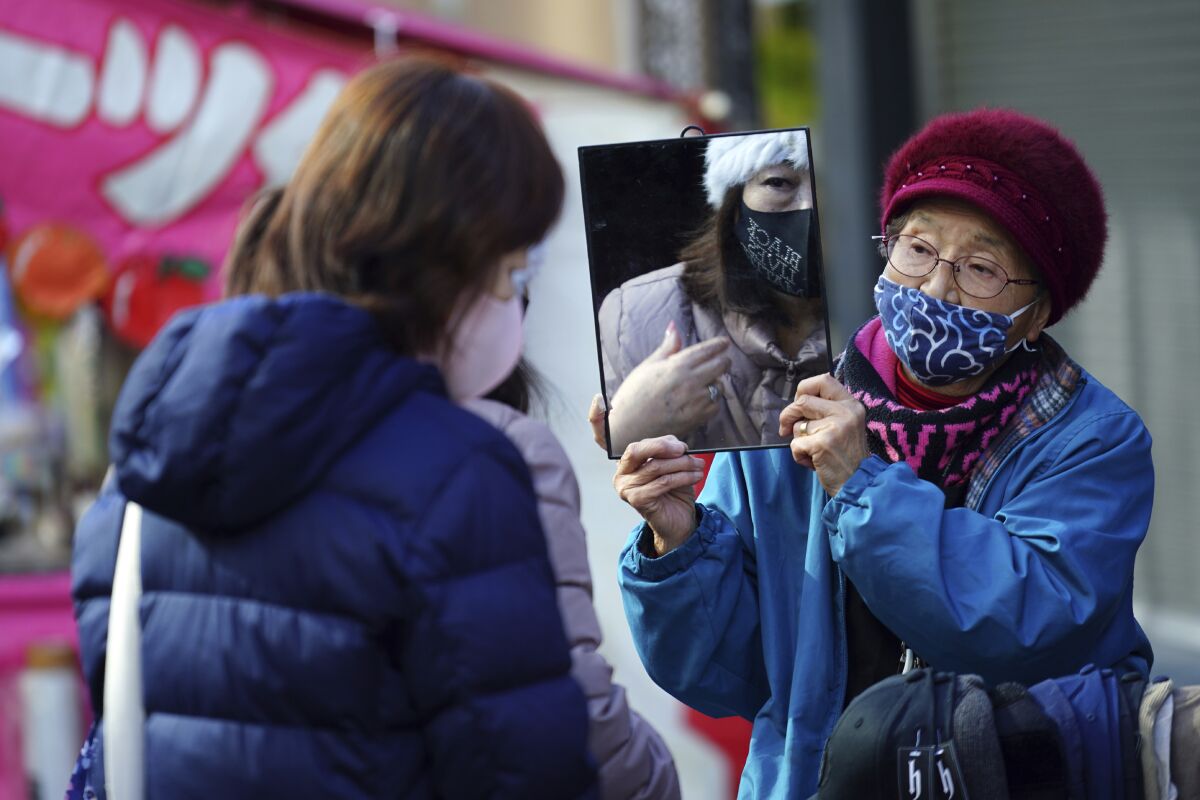 A shopper wearing a protective mask to help curb the spread of the coronavirus uses a mirror as she tries on a hat in a shopping street in Tokyo Thursday, Jan. 14, 2021. The Japanese capital confirmed more than 1500 new coronavirus cases on Thursday. (AP Photo/Eugene Hoshiko)