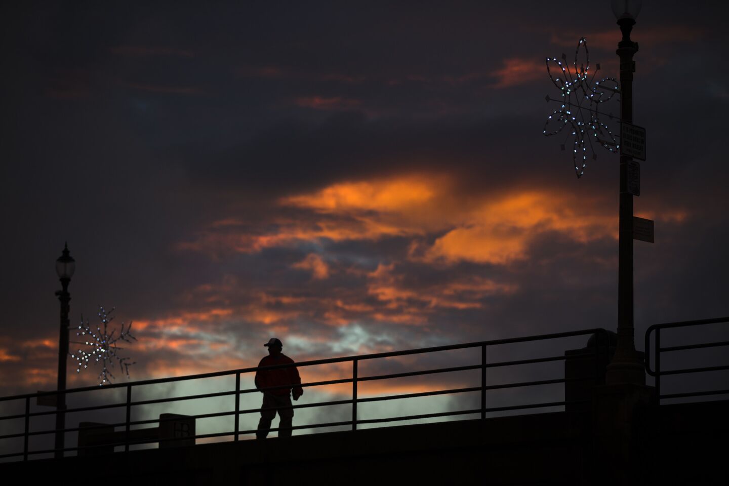 A man is silhouetted against a dramatic sky at sunset while walking on the Huntington Beach pier.