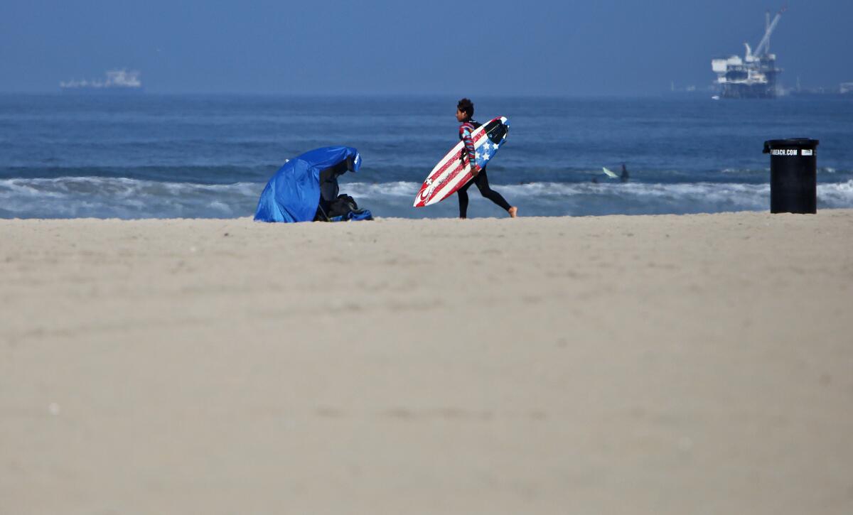 A surfer carrying a surfboard crosses the almost empty beach to catch some waves in Huntington Beach on May 2.