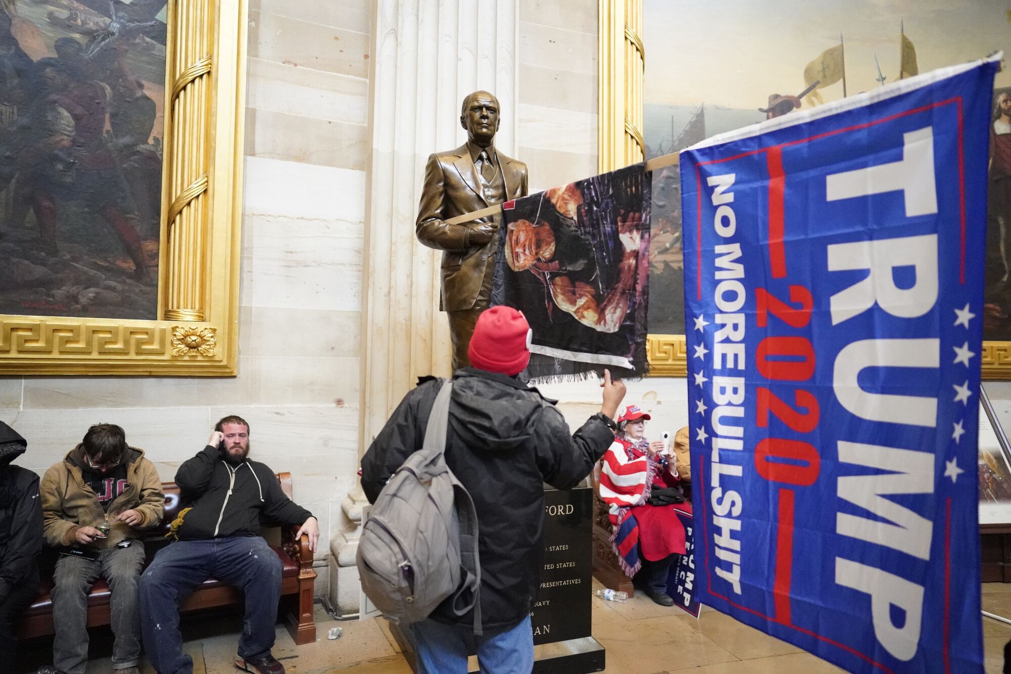 Trump supporters sit on a bench and have stuck a Trump flag reading "No more bullshit" into a statue.