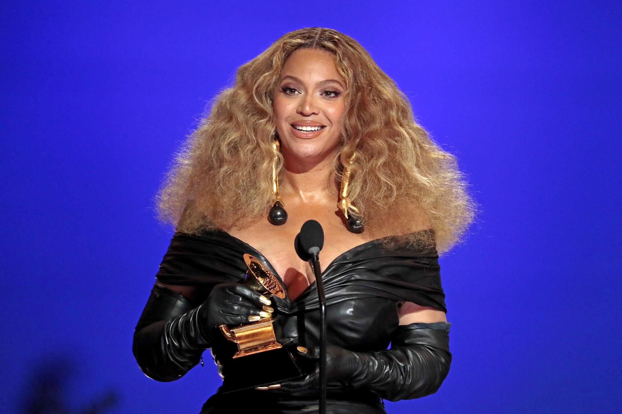 Beyoncé in a black, off-shoulder dress, holding a Grammy Award