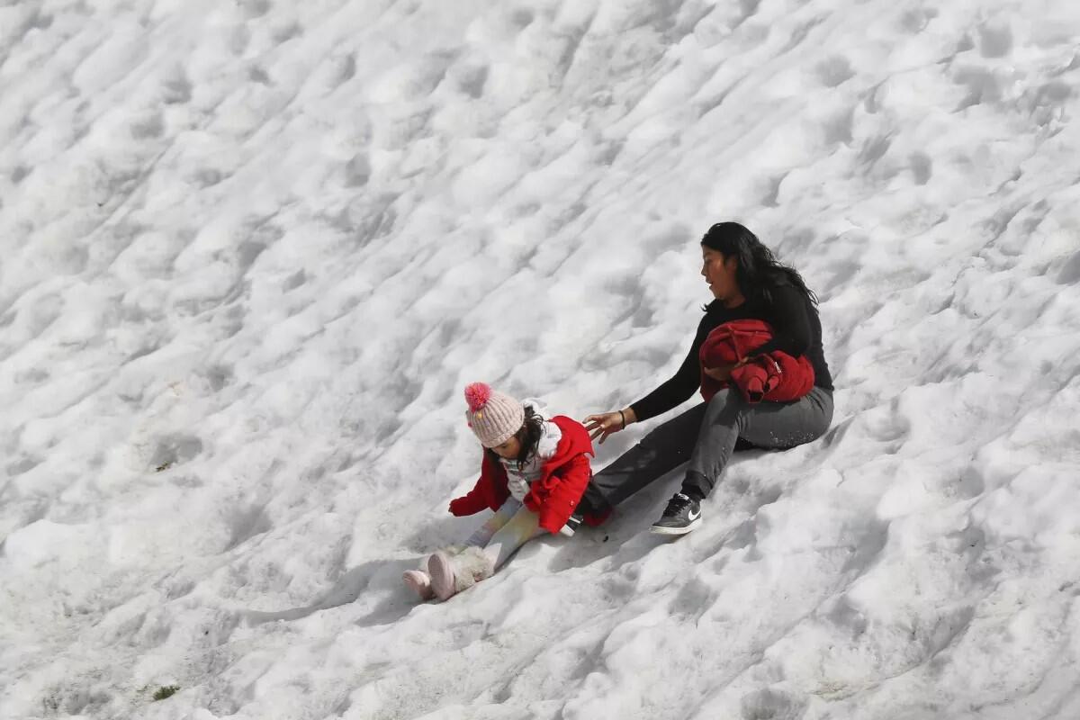 mujer sostiene a una niña mientras juegan en una carretera nevada cerca del monte Baldy.