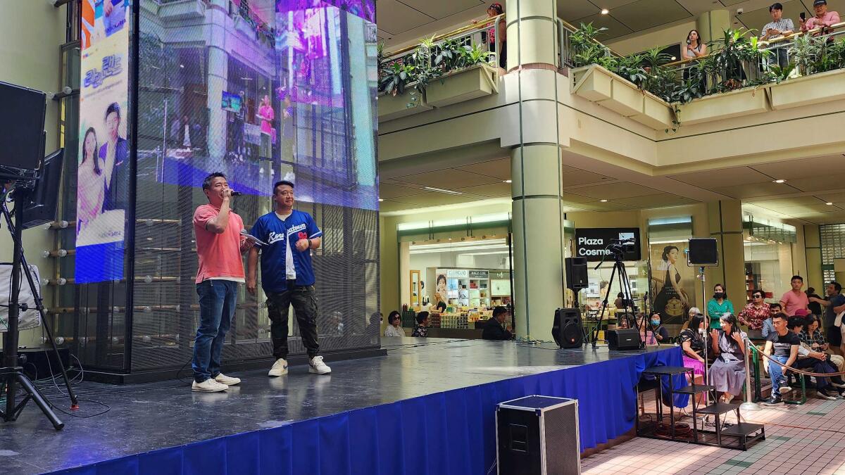 Two people  stand onstage at a mall.