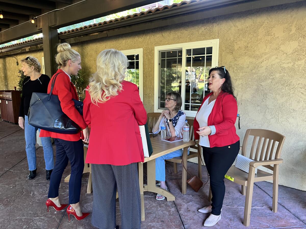 Women behind a table greet two women in red blazers