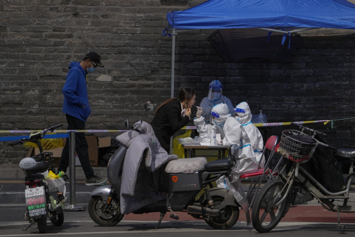 A woman leans toward a worker in a white protective suit holding a swab under a blue tent on a street