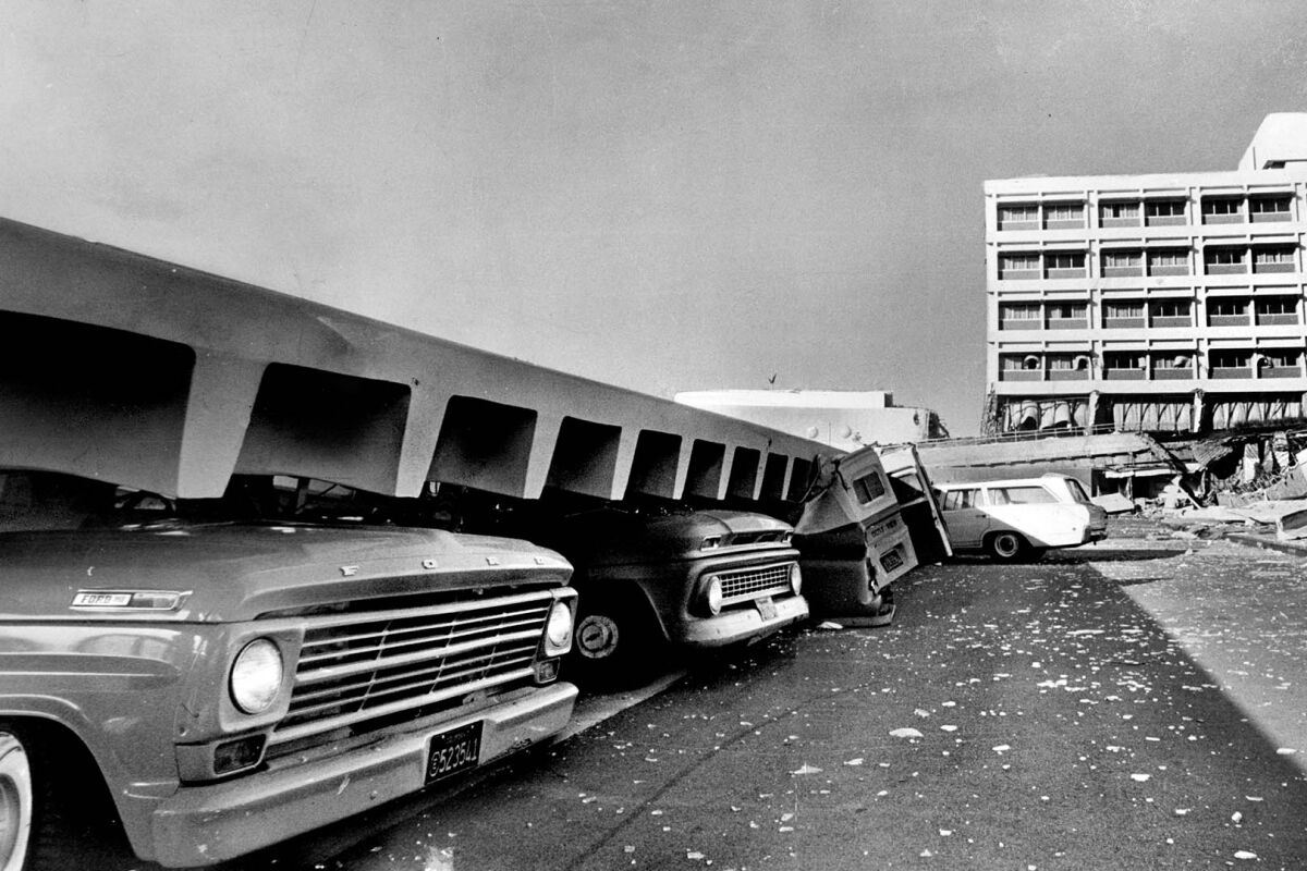 The hoods of cars stick out from the edge of a collapsed floor or wall.